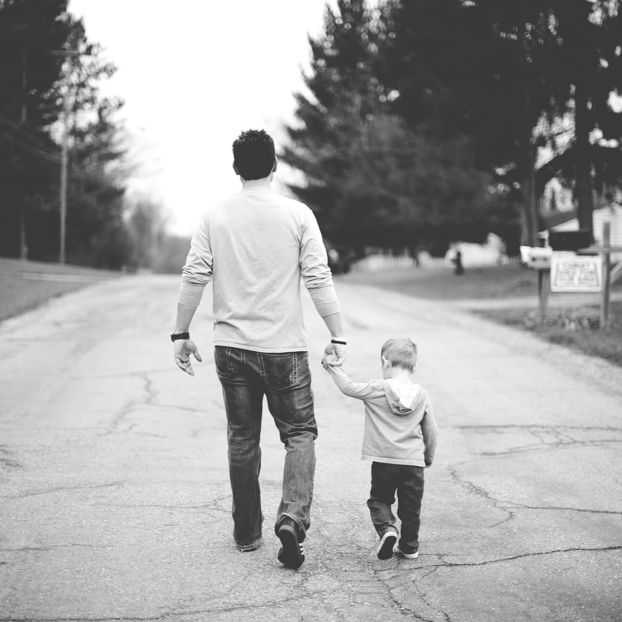 A father holding his son's hand while they both walk away down the street